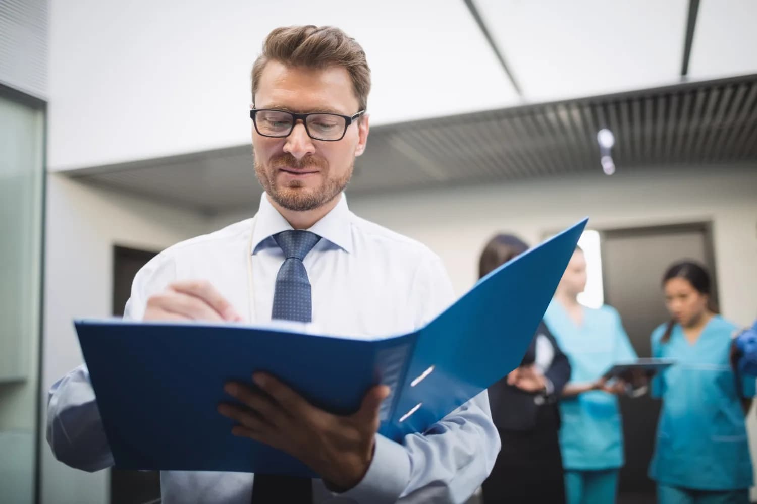 Responsable des ressources humaines consultant un dossier, équipe soignante en arrière-plan